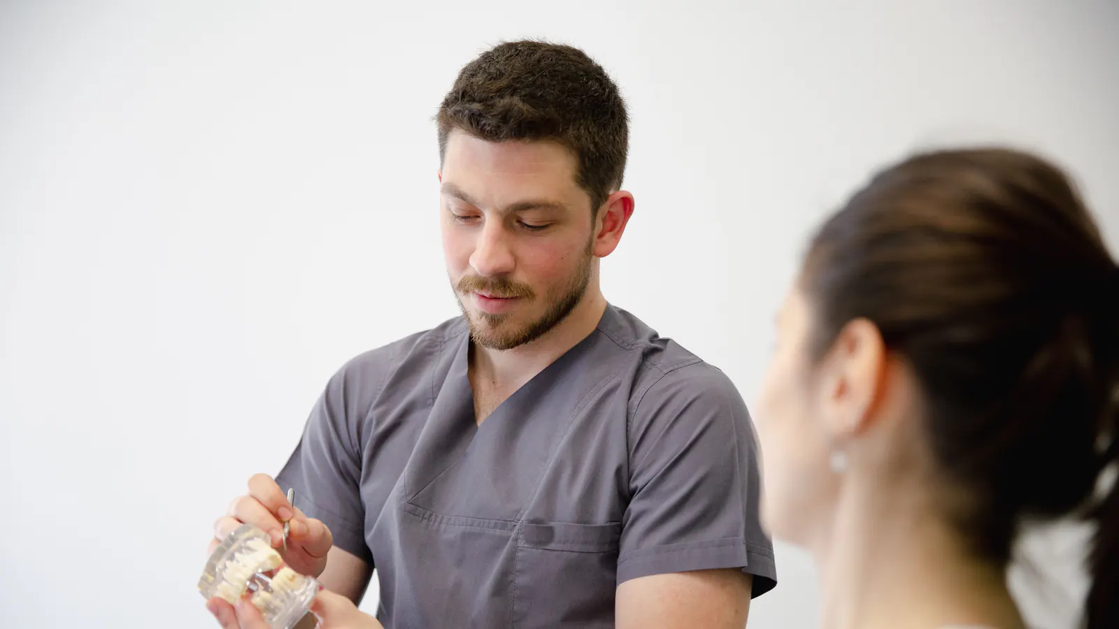 A dentist shows a patient a dental implant model during a consultation.