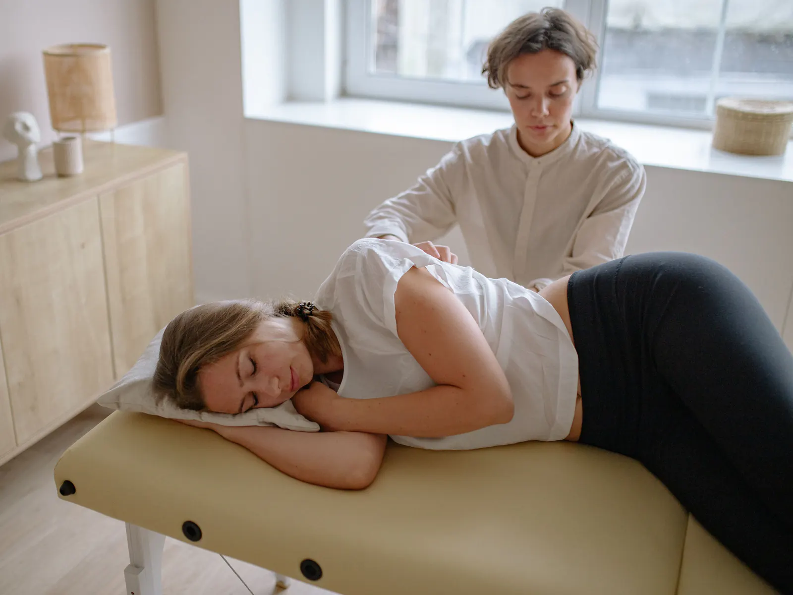 A practitioner works on the back of a patient lying on her side on a treatment table.