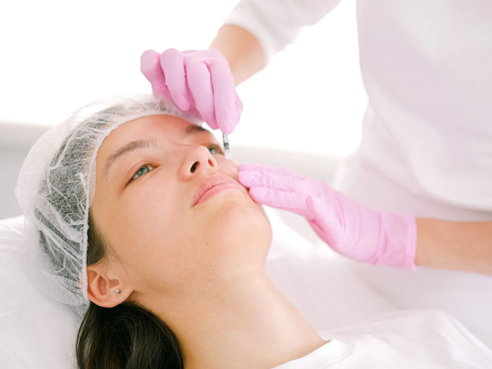 A clinician in gloves treats a patient’s face with a fine needle during a skin procedure.