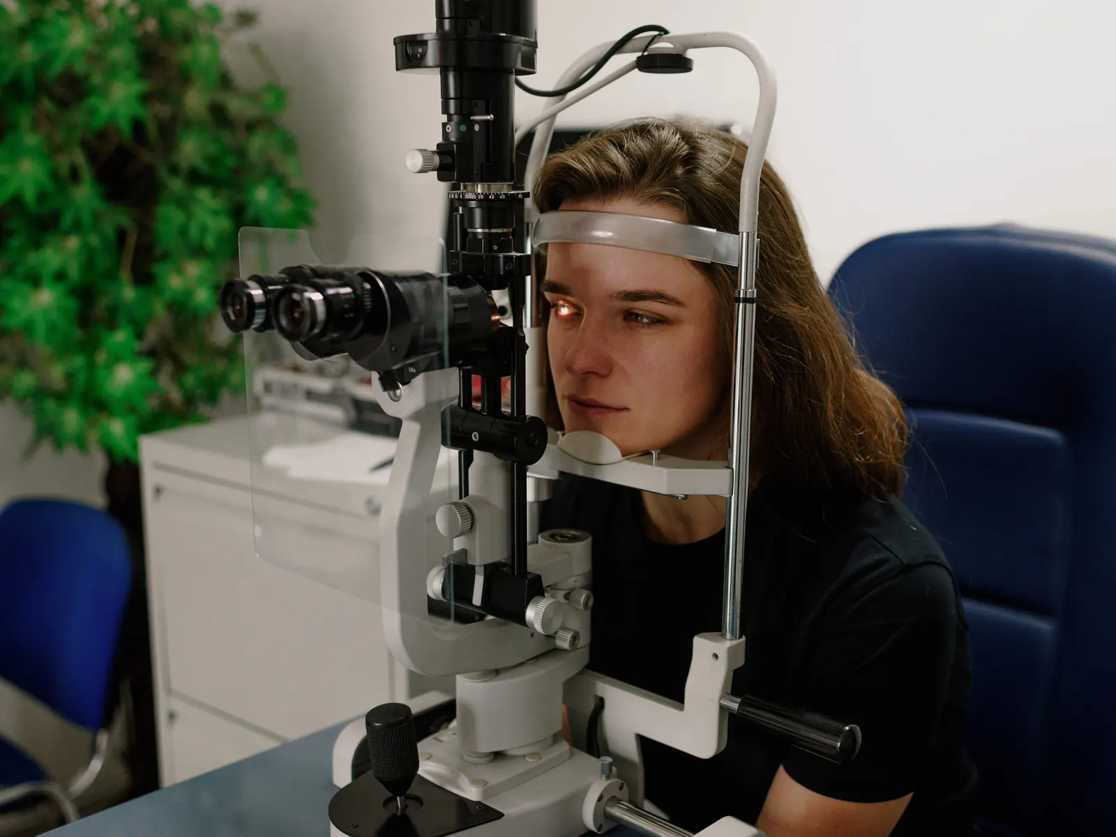 A patient rests at a slit lamp with a light on one eye during an eye exam.